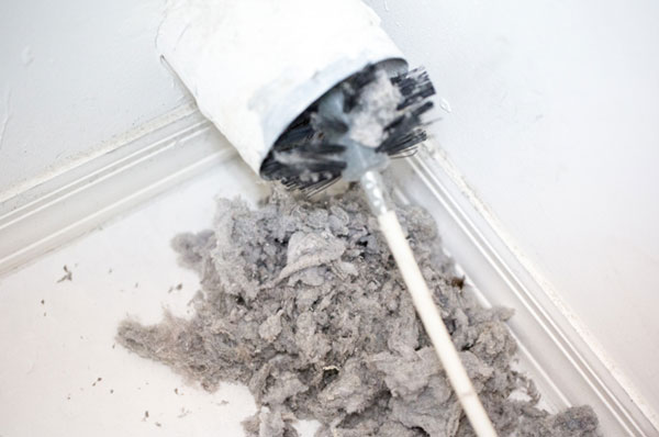 Dryer vent in a home being cleaned out with a round brush. There is a large pile of lint that has been removed from the vent on a white tiled floor.